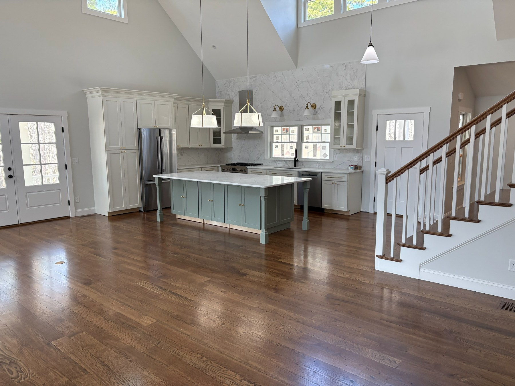Vaulted great room with glossy refinished hardwood floor, open kitchen, and staircase